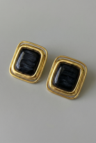 Pair of gold earrings with black stones on a gray background