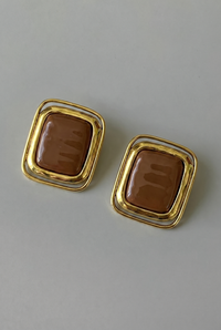 Pair of gold-framed brown square earrings on a light gray background
