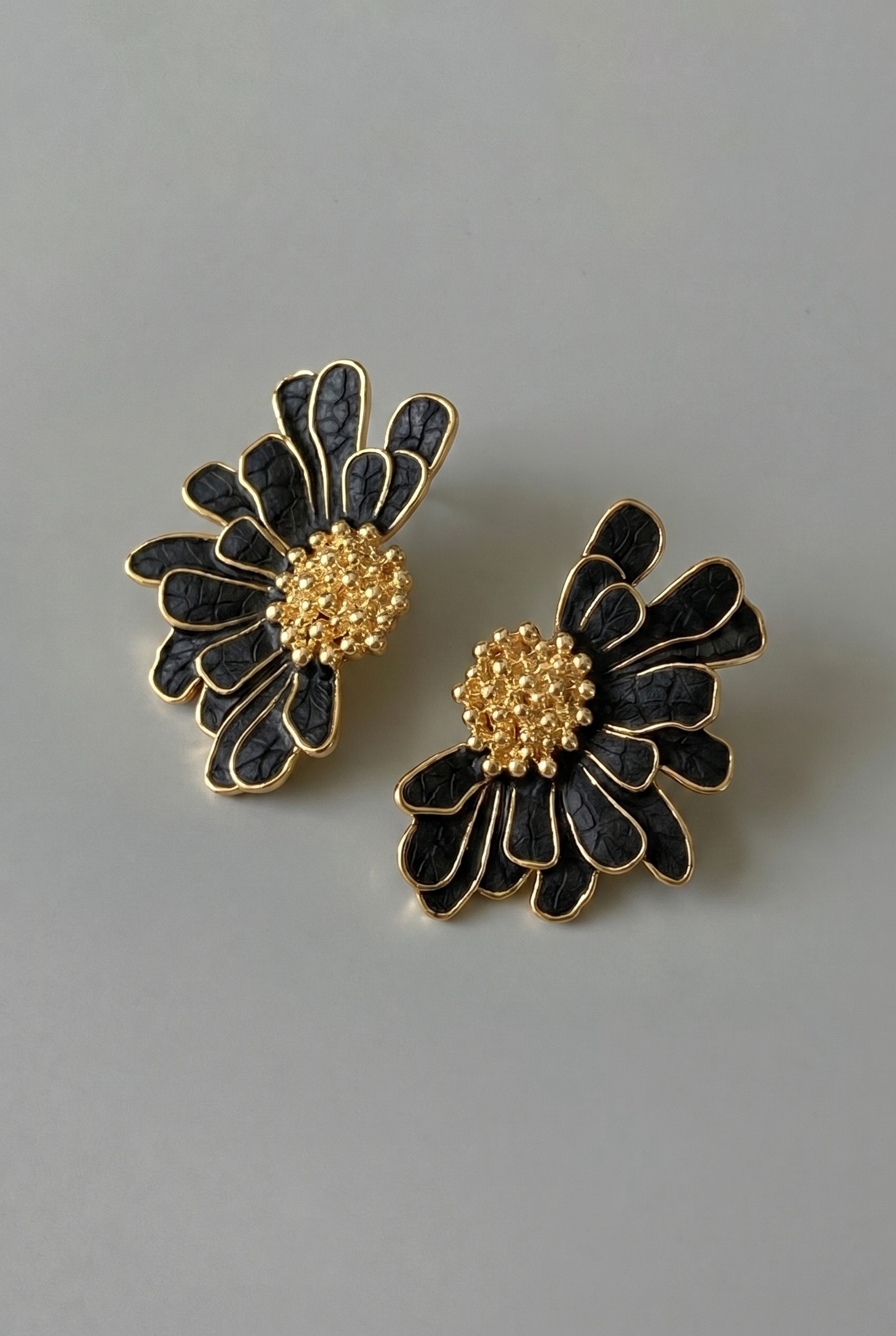 Pair of black and gold floral earrings on a gray background