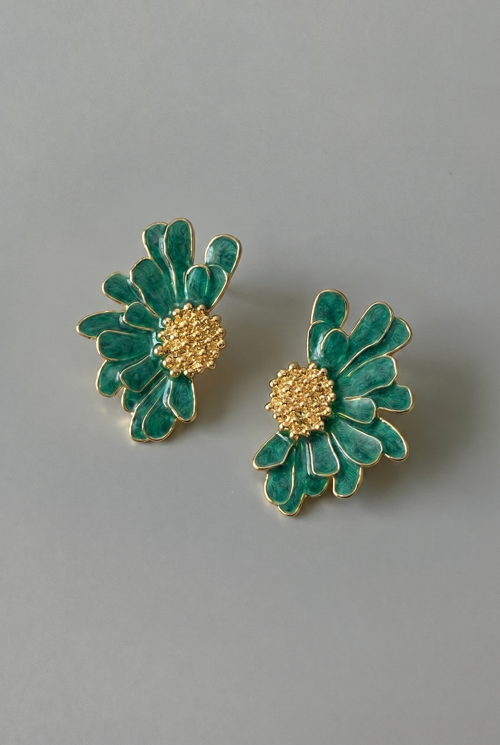 Pair of green floral earrings with gold centers on a gray background