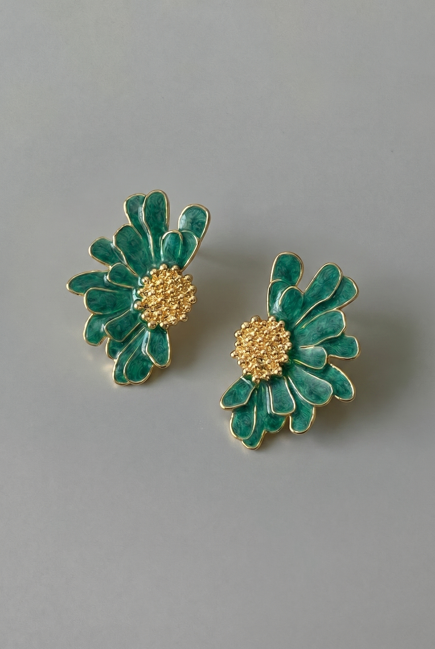 Pair of green floral earrings with gold centers on a gray background