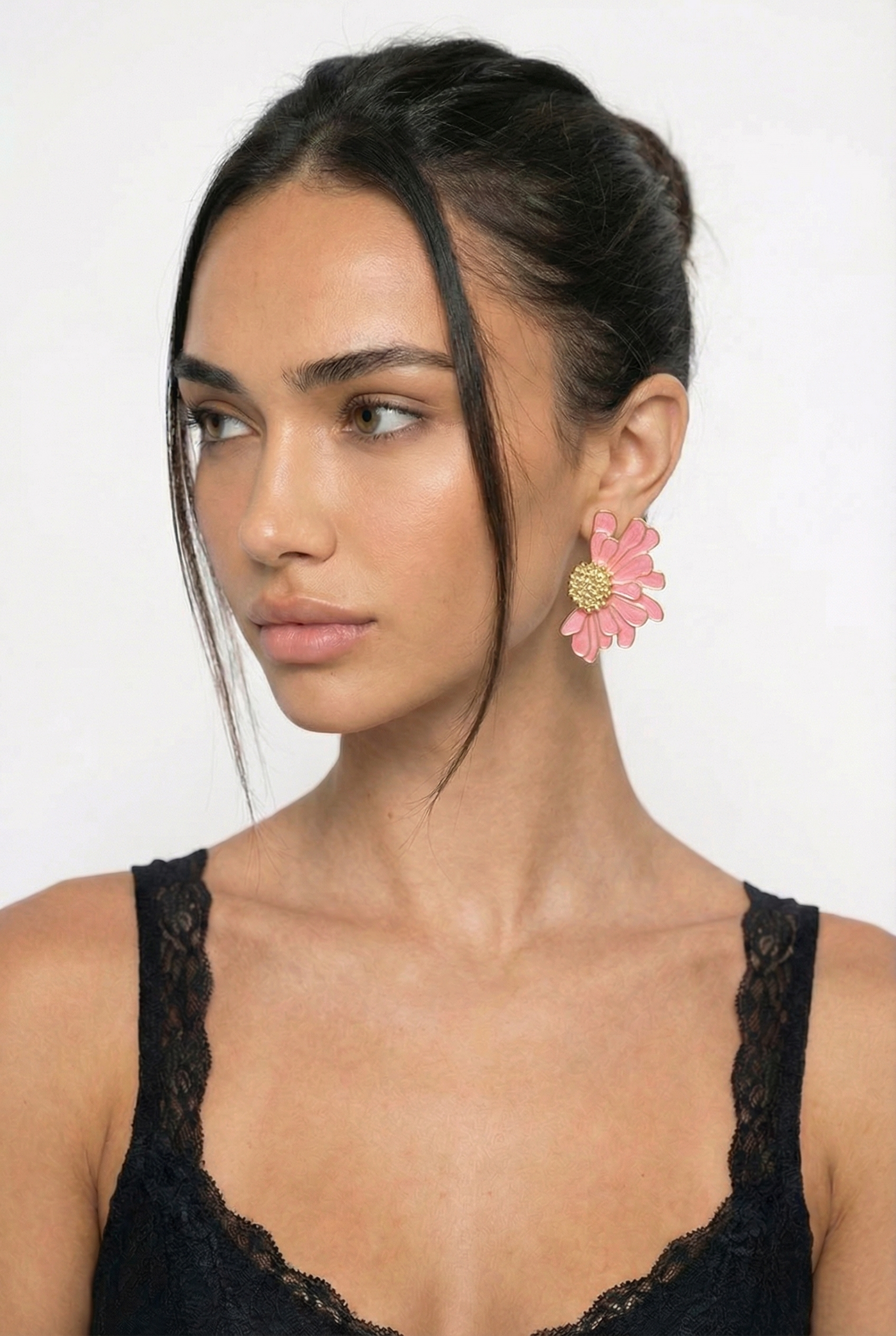 Woman wearing a black lace top with pink floral earrings against a white background