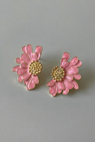 Pink flower-shaped earrings with gold centers on a gray background
