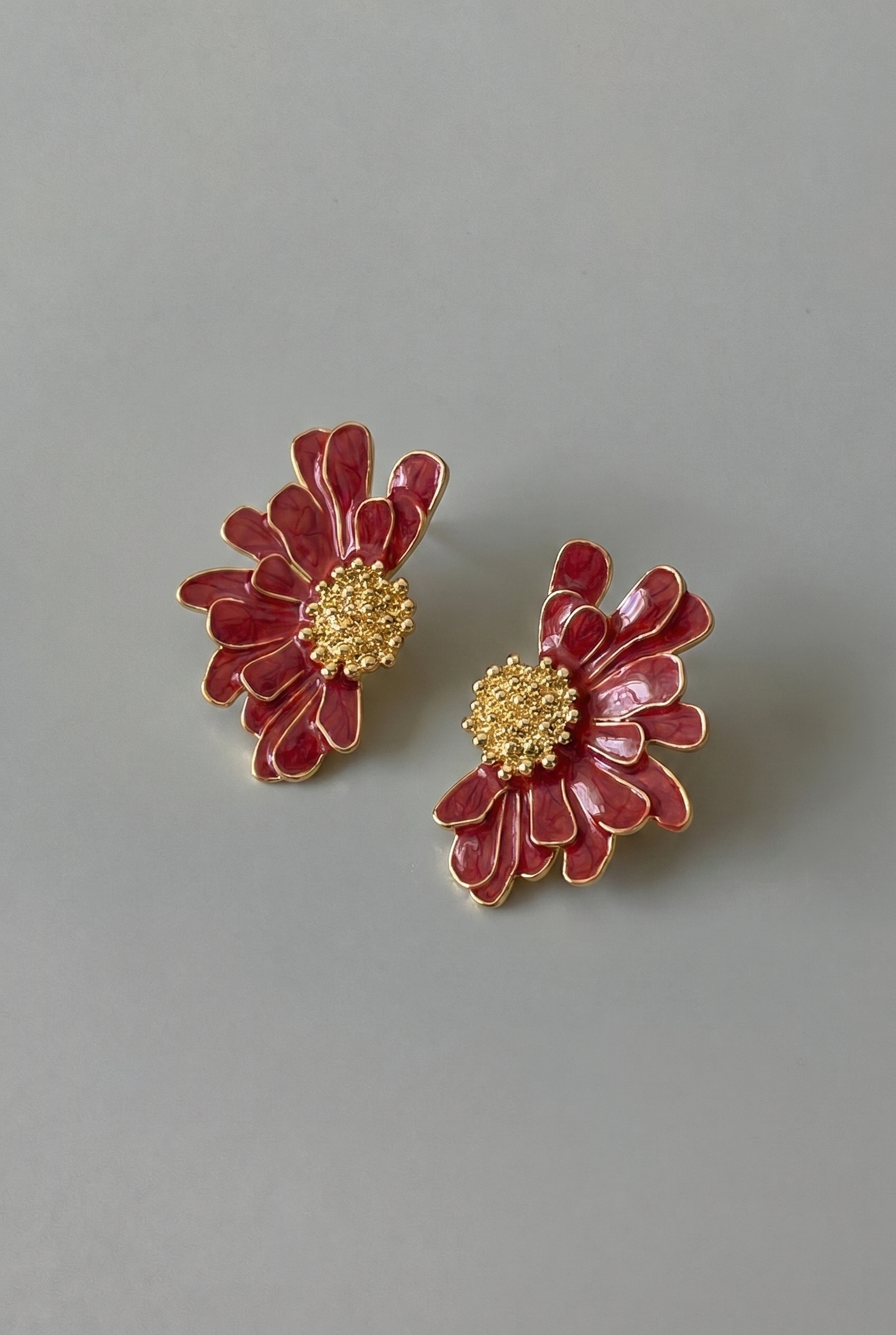 Pair of red floral earrings with gold centers on a gray background