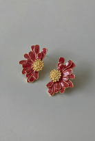 Pair of red floral earrings with gold centers on a gray background