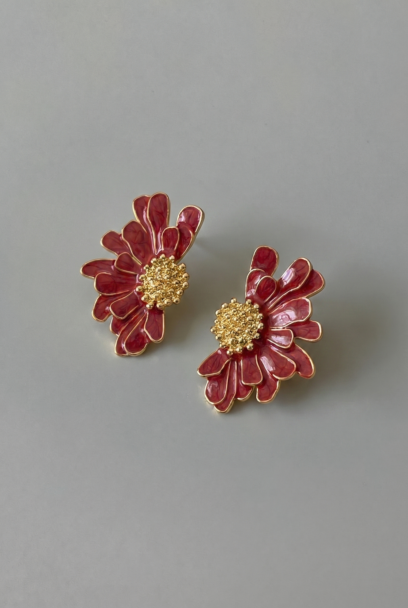 Pair of red floral earrings with gold centers on a gray background