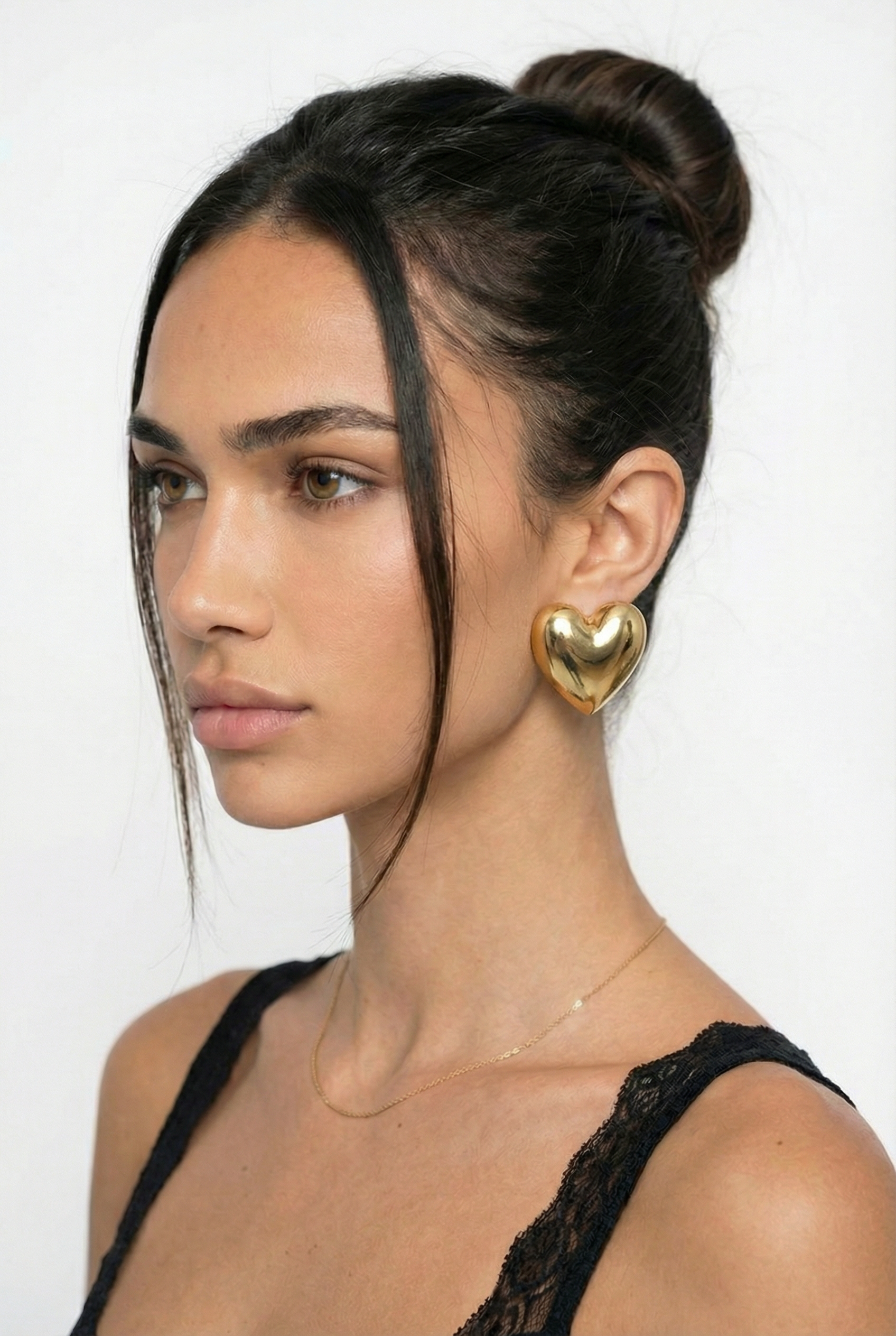 Woman with a stylish hair bun wearing gold heart-shaped earrings against a white background