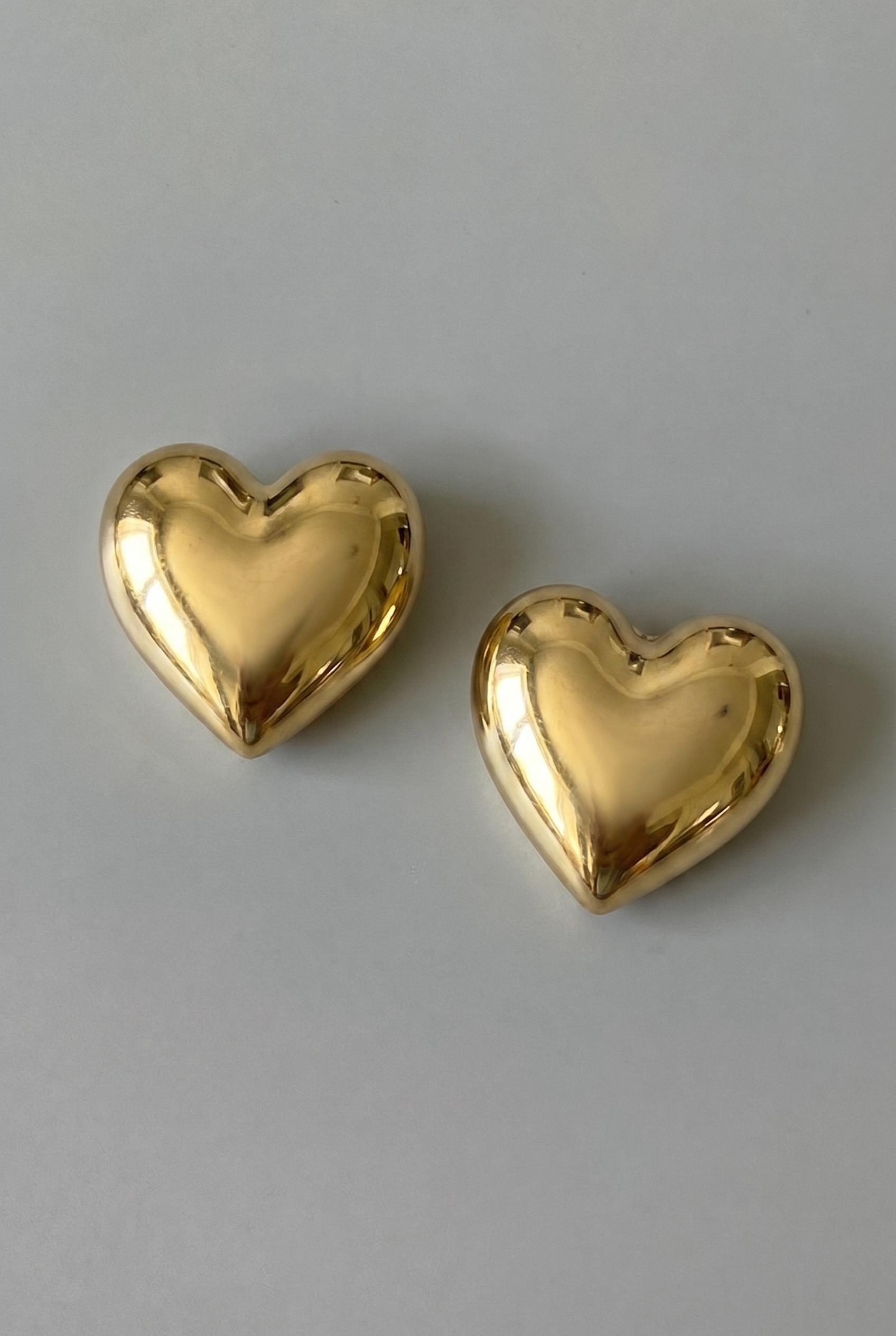 Two gold heart-shaped earrings on a gray background