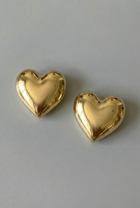 Two gold heart-shaped earrings on a gray background