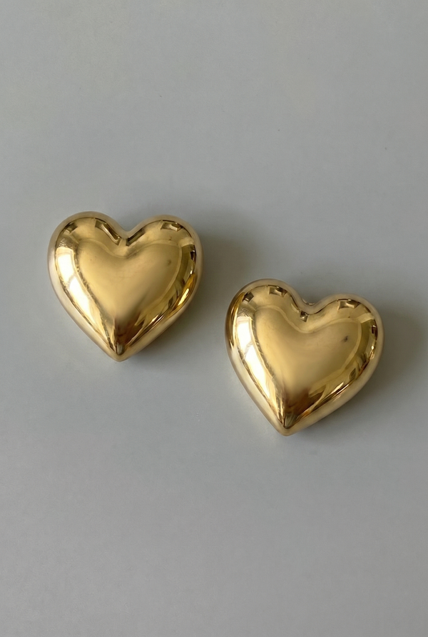 Two gold heart-shaped earrings on a gray background