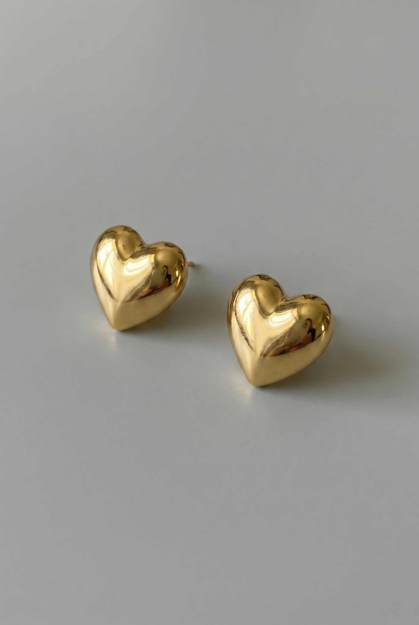 Gold heart-shaped earrings on a gray background