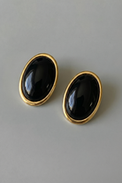 Pair of black oval earrings with gold rims on a gray background