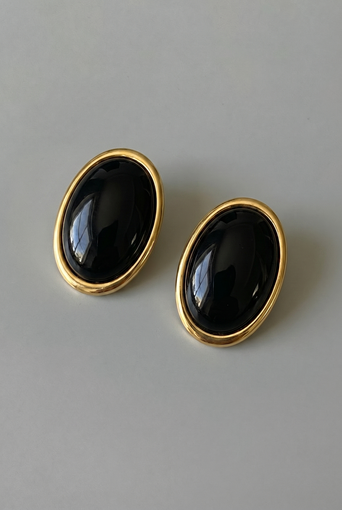 Pair of black oval earrings with gold rims on a gray background