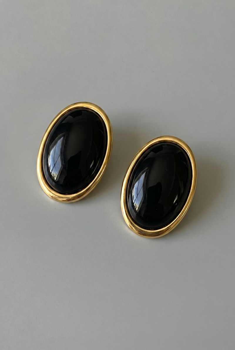 Pair of black oval earrings with gold rims on a gray background