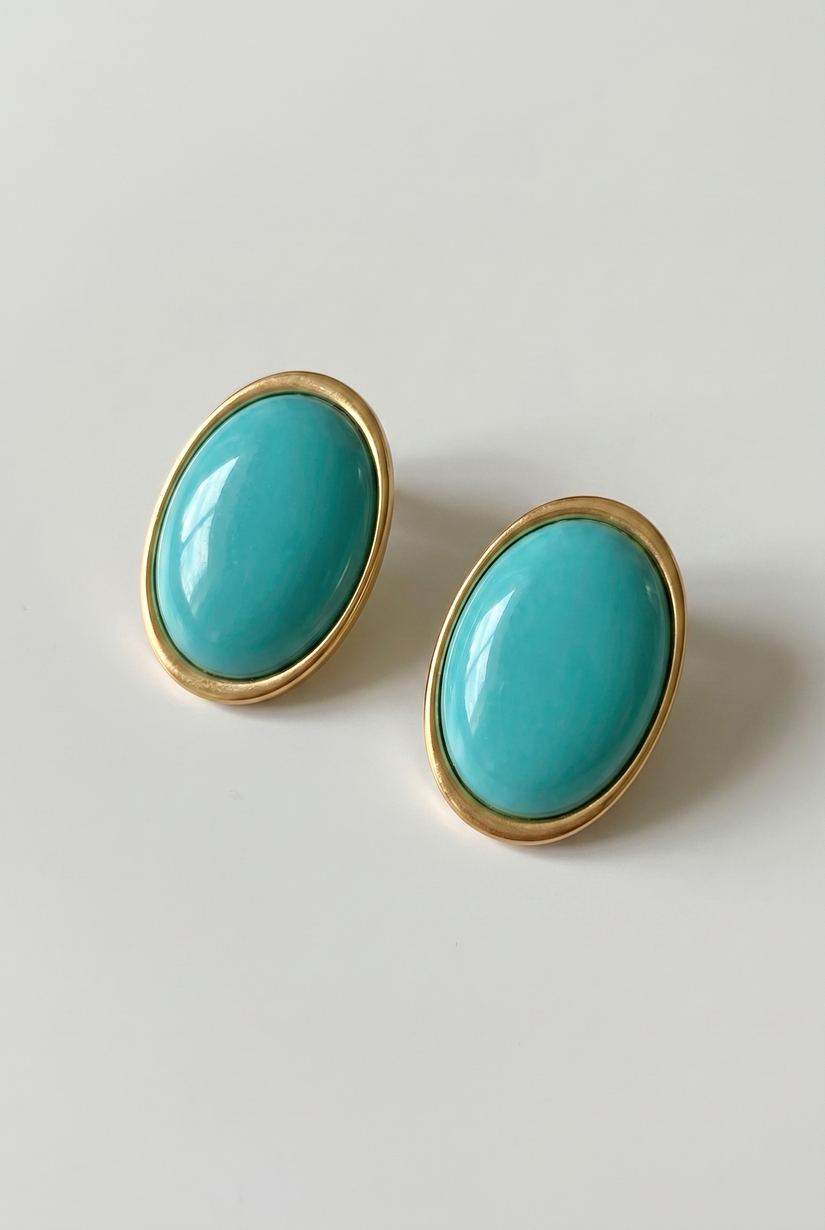 Turquoise earrings with gold frames on a light gray background