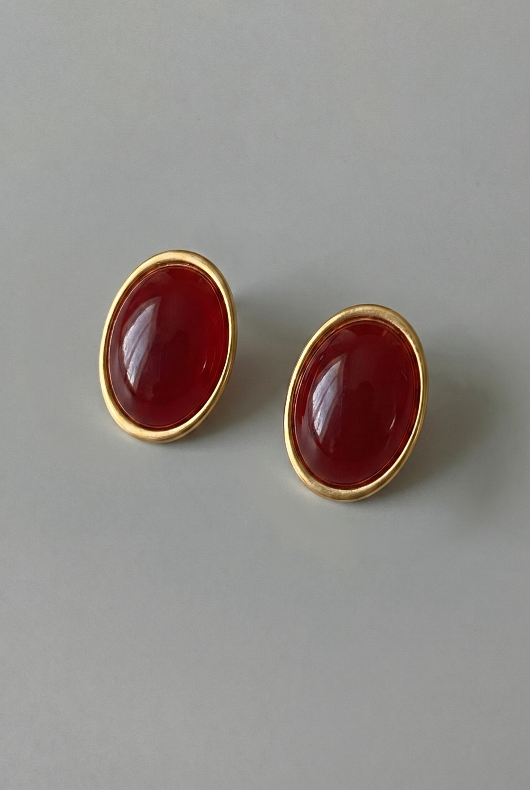 Pair of gold earrings with red stones on a gray background