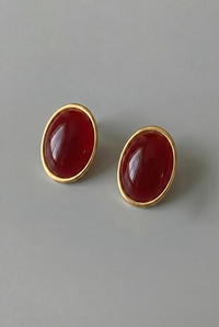 Pair of gold earrings with red stones on a gray background