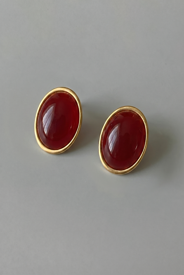 Pair of gold earrings with red stones on a gray background