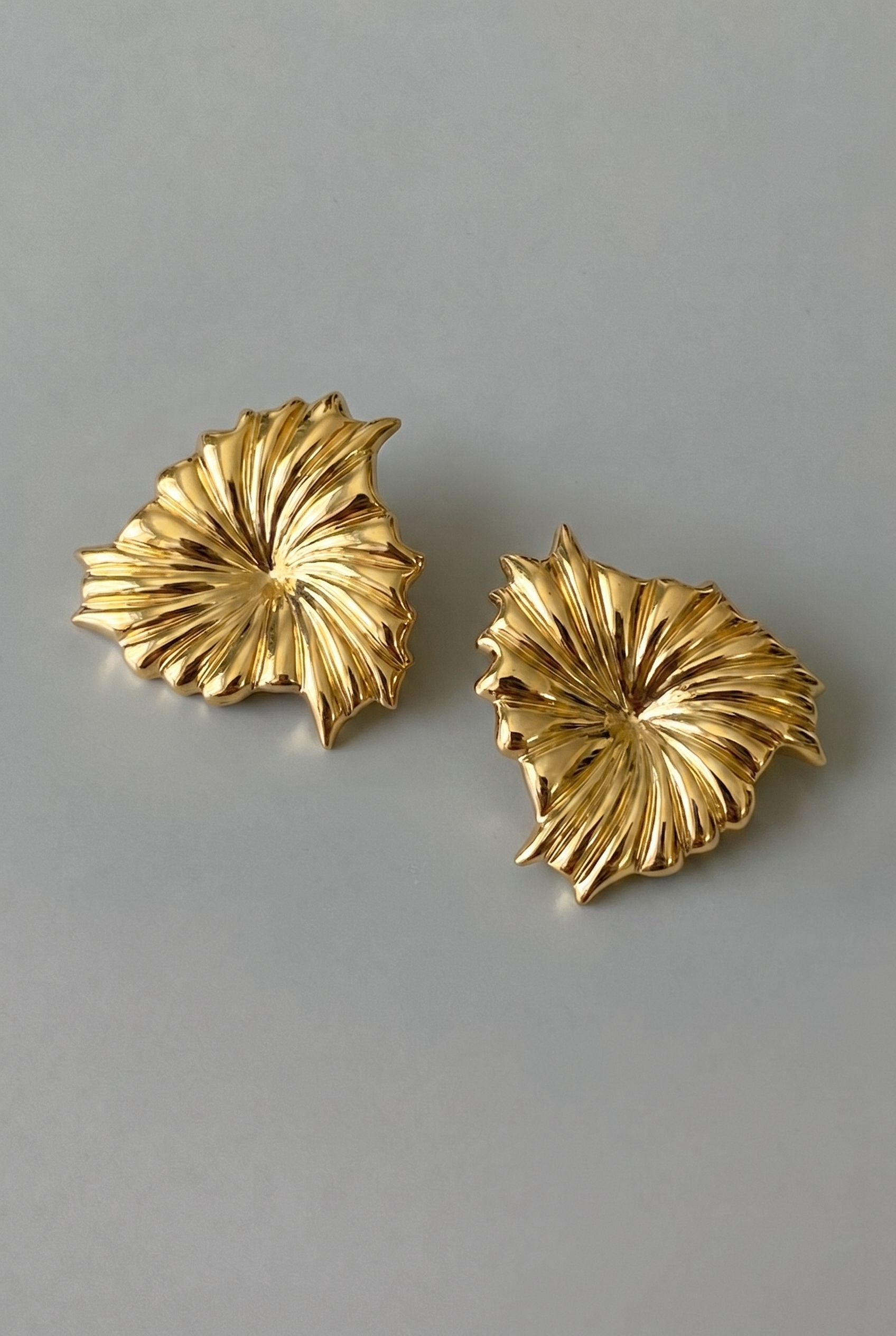 Pair of gold leaf-shaped earrings on a gray background