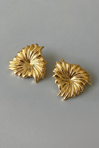 Pair of gold leaf-shaped earrings on a gray background