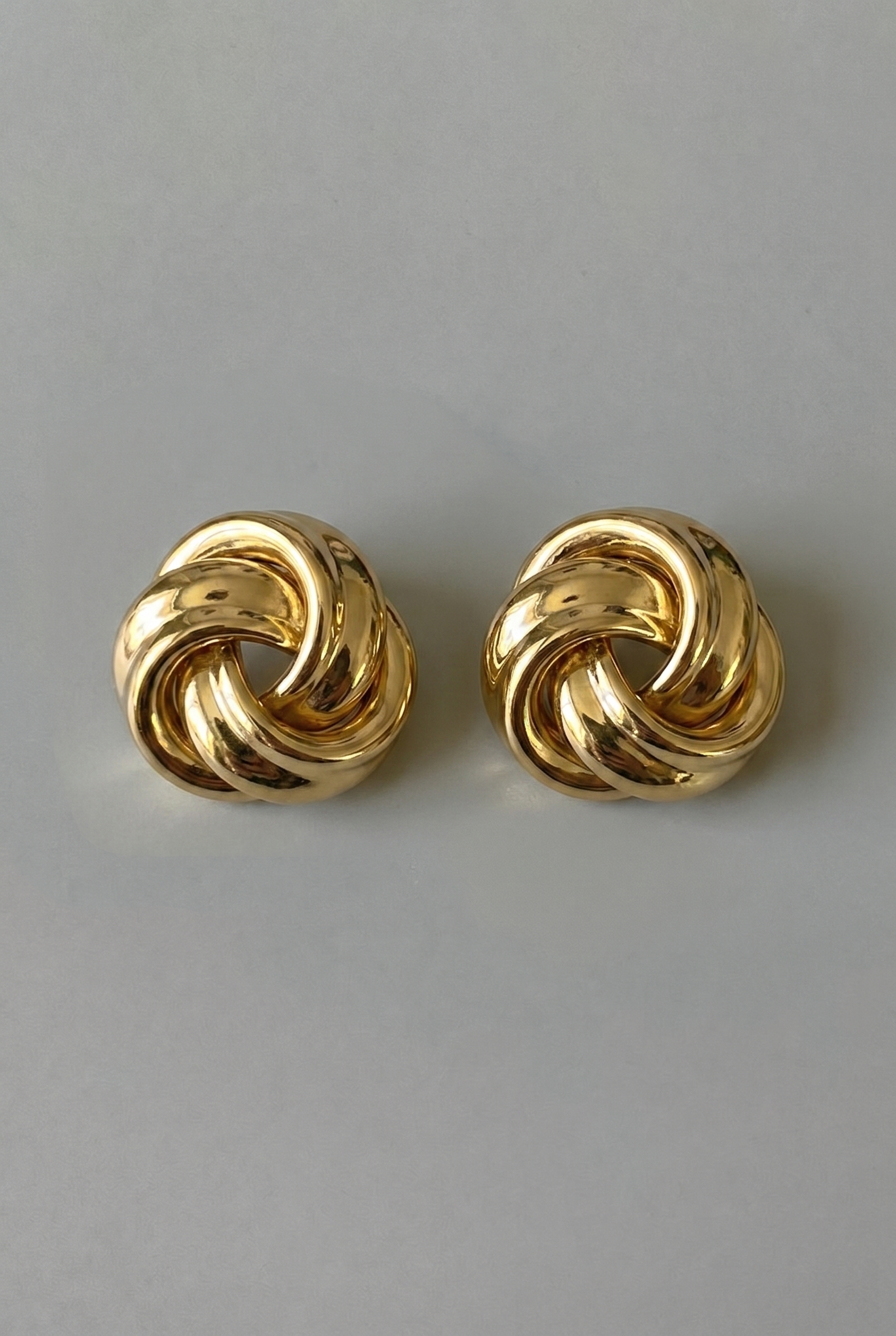 Pair of gold knot earrings on a gray background