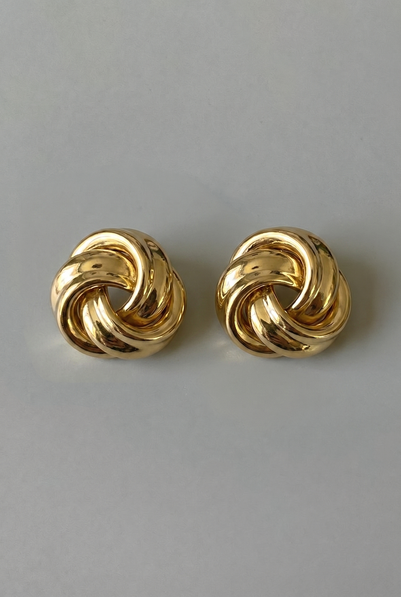 Pair of gold knot earrings on a gray background