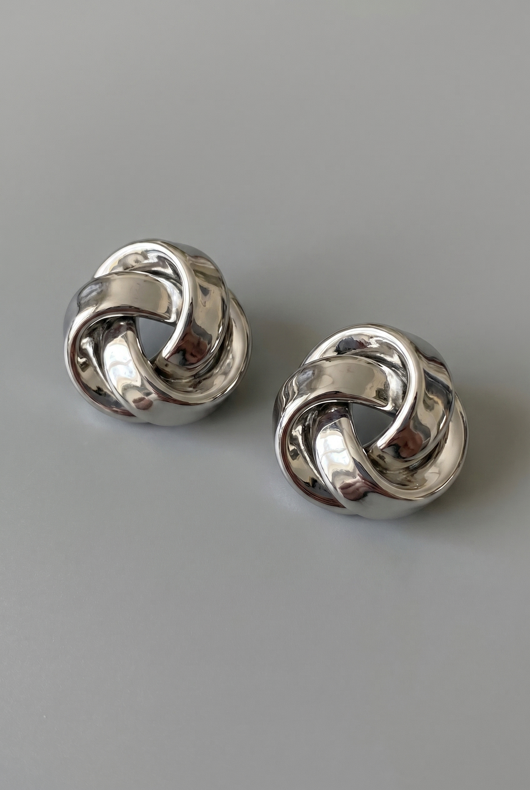 Pair of silver knot earrings on a gray background