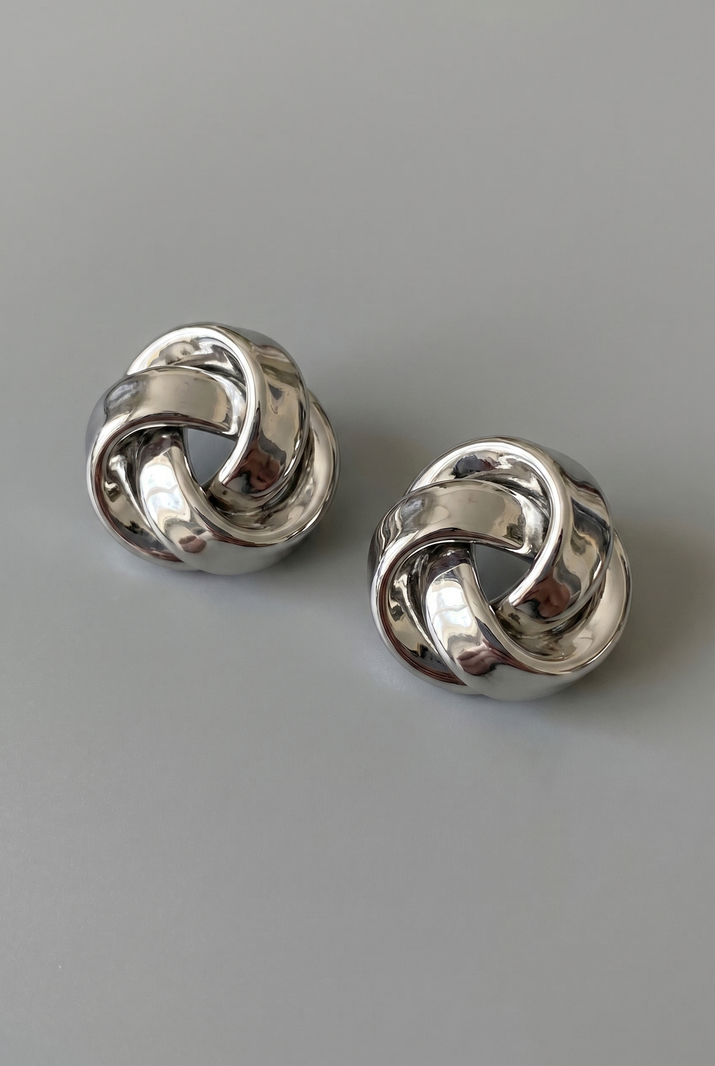 Pair of silver knot earrings on a gray background