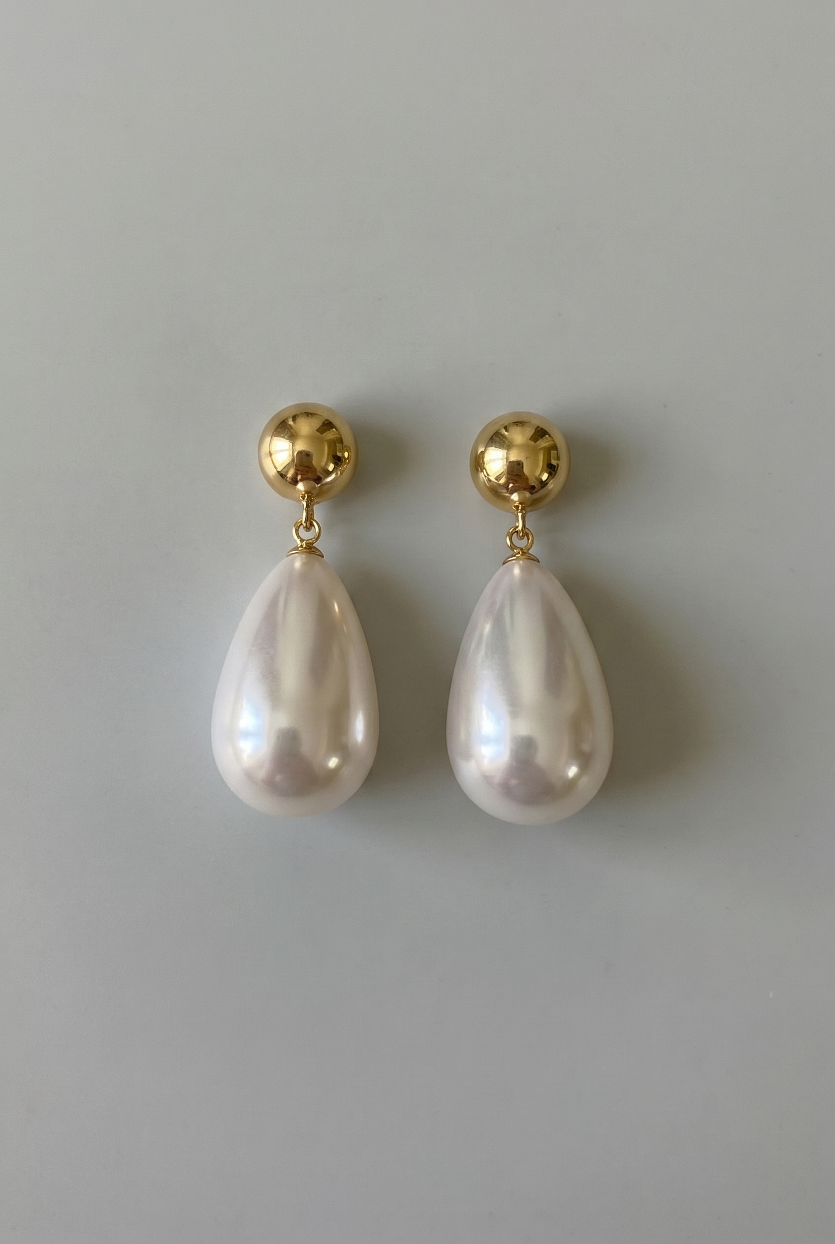 Pearl earrings with gold posts on a gray background