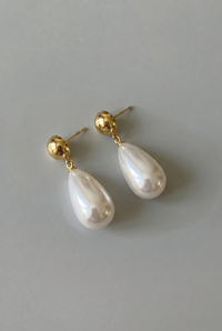 Pearl earrings with gold posts on a light gray background
