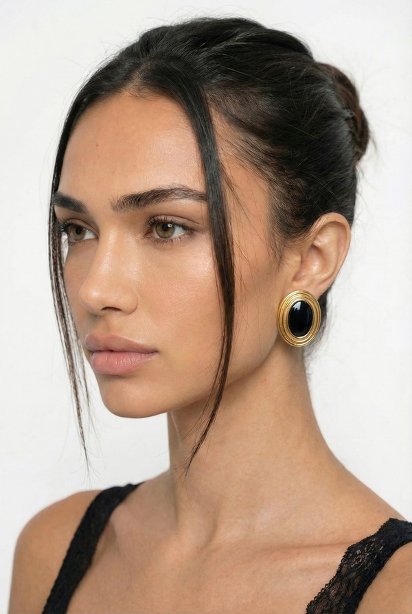 Close-up of a woman wearing gold earrings with black stones on a white background
