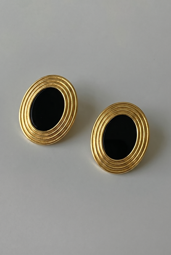 Pair of gold earrings with black centers on a gray background