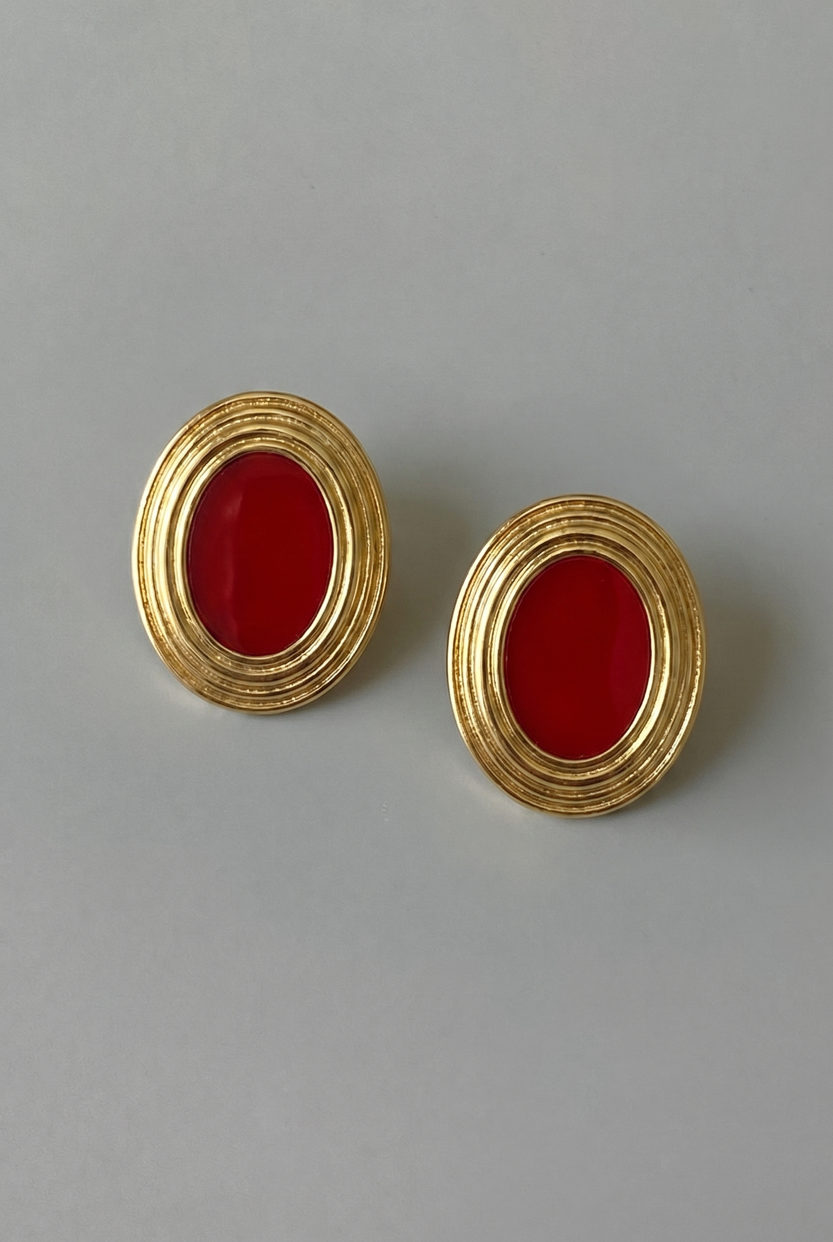 Pair of gold earrings with red stones on a gray background