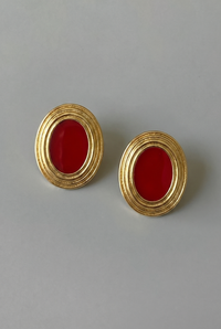 Pair of gold earrings with red stones on a gray background