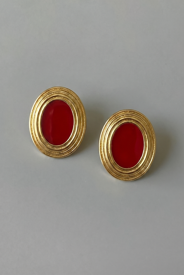 Pair of gold earrings with red stones on a gray background