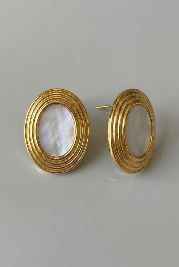 Gold hoop earrings with a central pearl-like stone on a light gray background