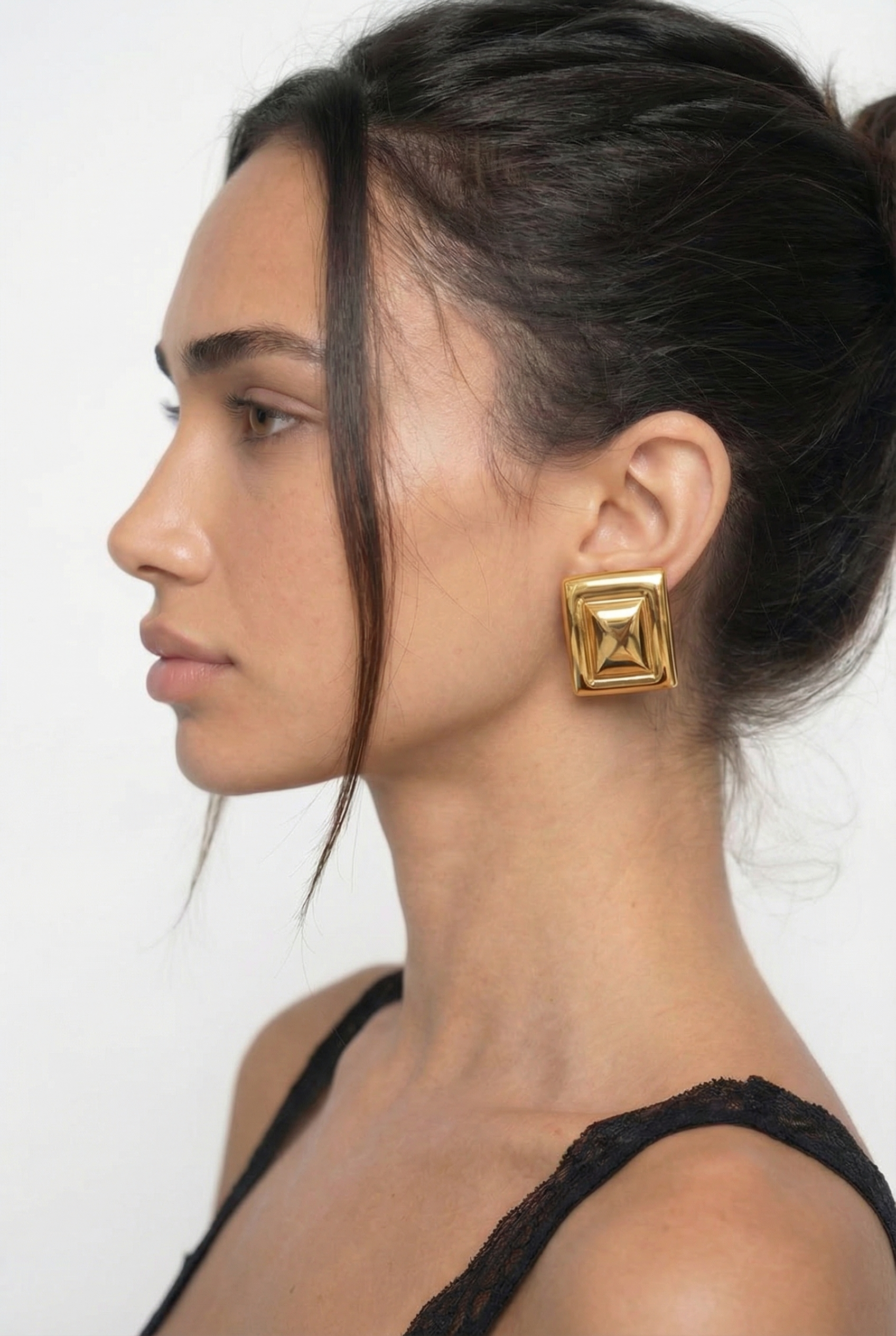 Woman wearing gold square earrings against a white background