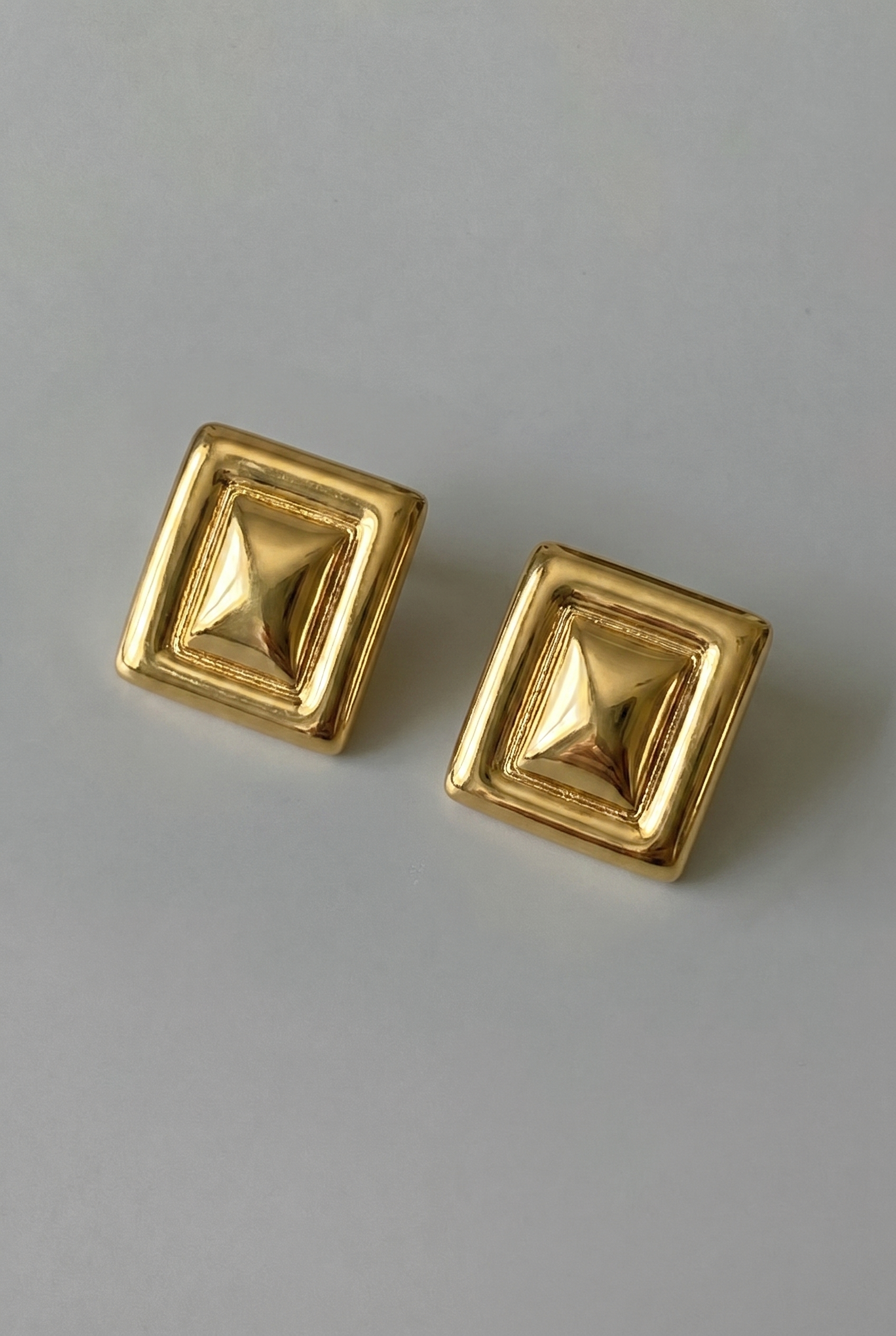 Pair of gold square earrings on a gray background