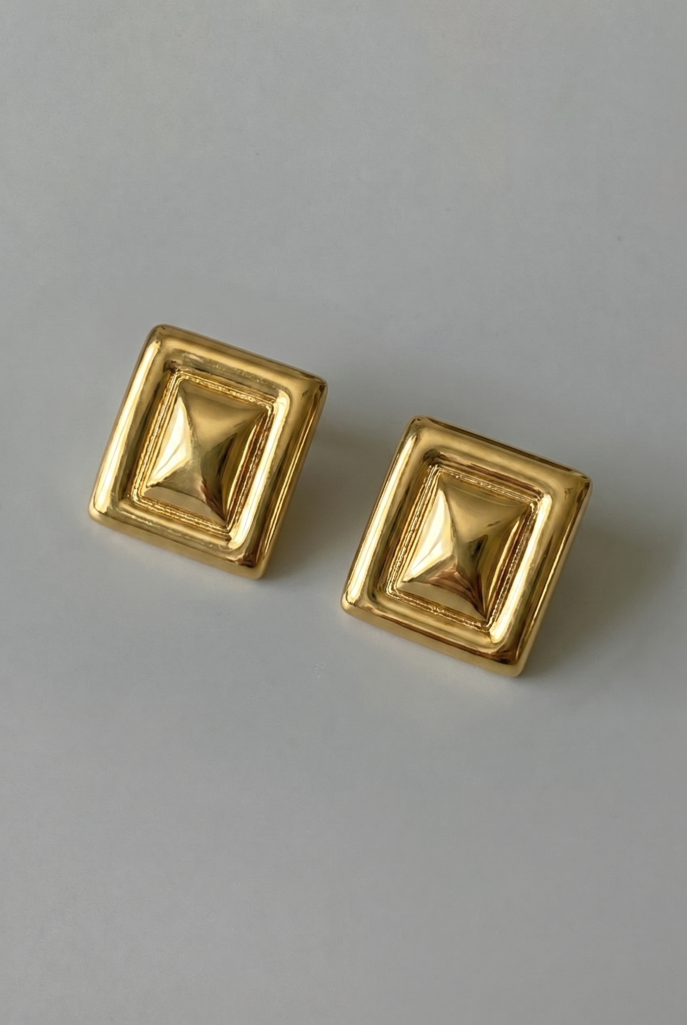 Pair of gold square earrings on a gray background
