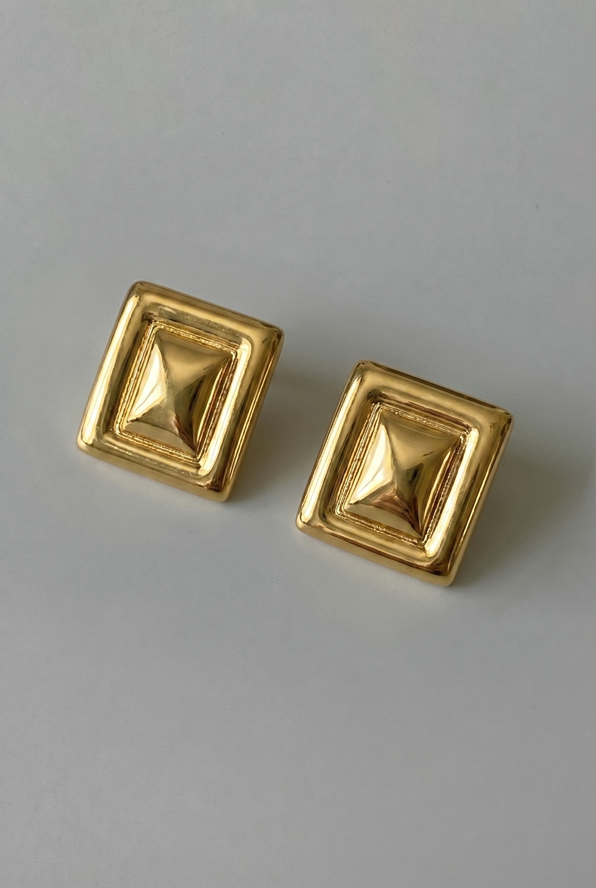 Pair of gold square earrings on a gray background