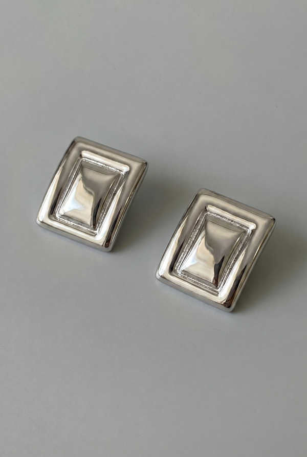 Pair of silver square earrings on a gray background