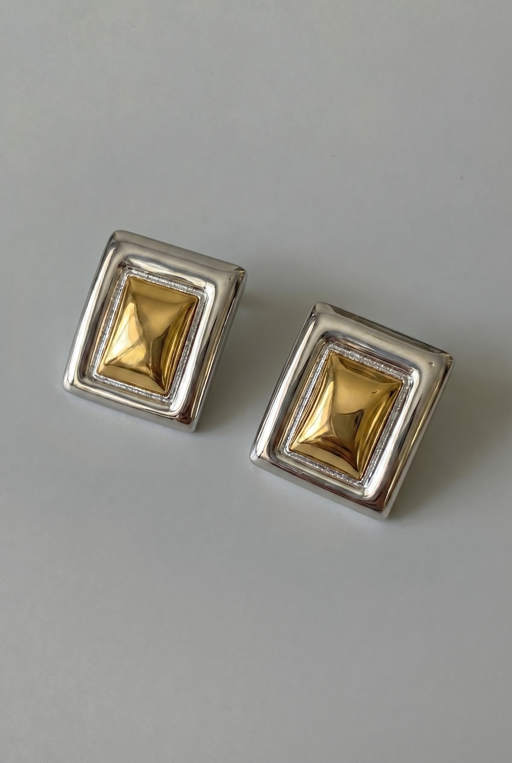 Pair of square gold earrings with silver frames on a gray background