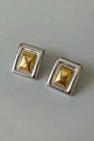 Pair of square gold earrings with silver frames on a gray background