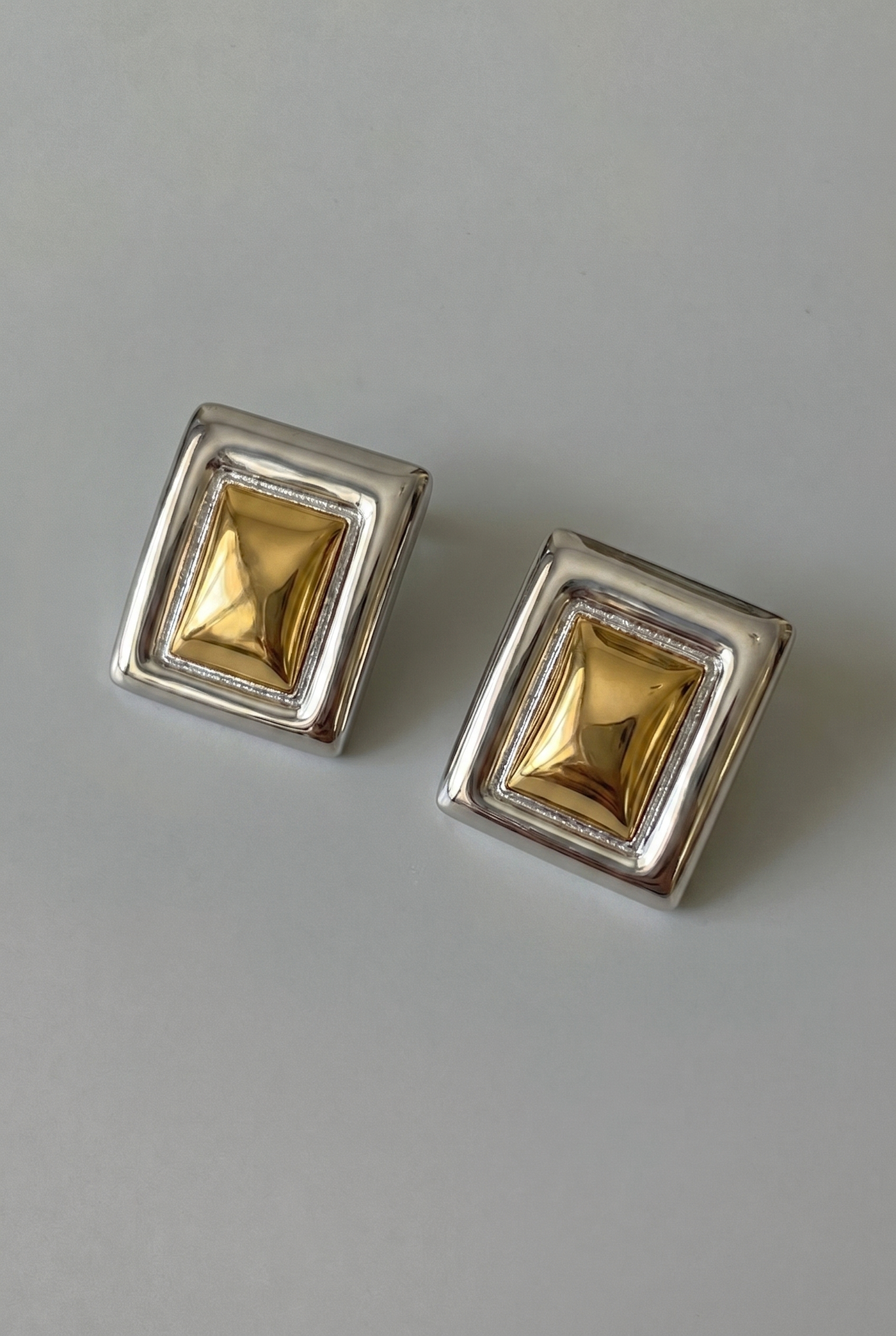 Pair of square gold earrings with silver frames on a gray background