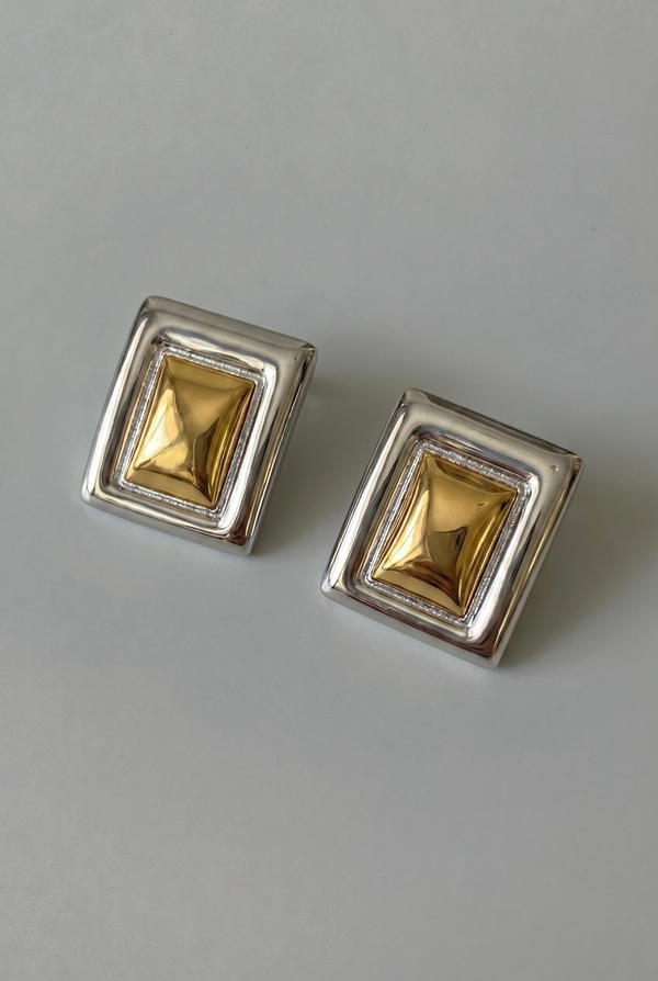 Pair of square gold earrings with silver frames on a gray background