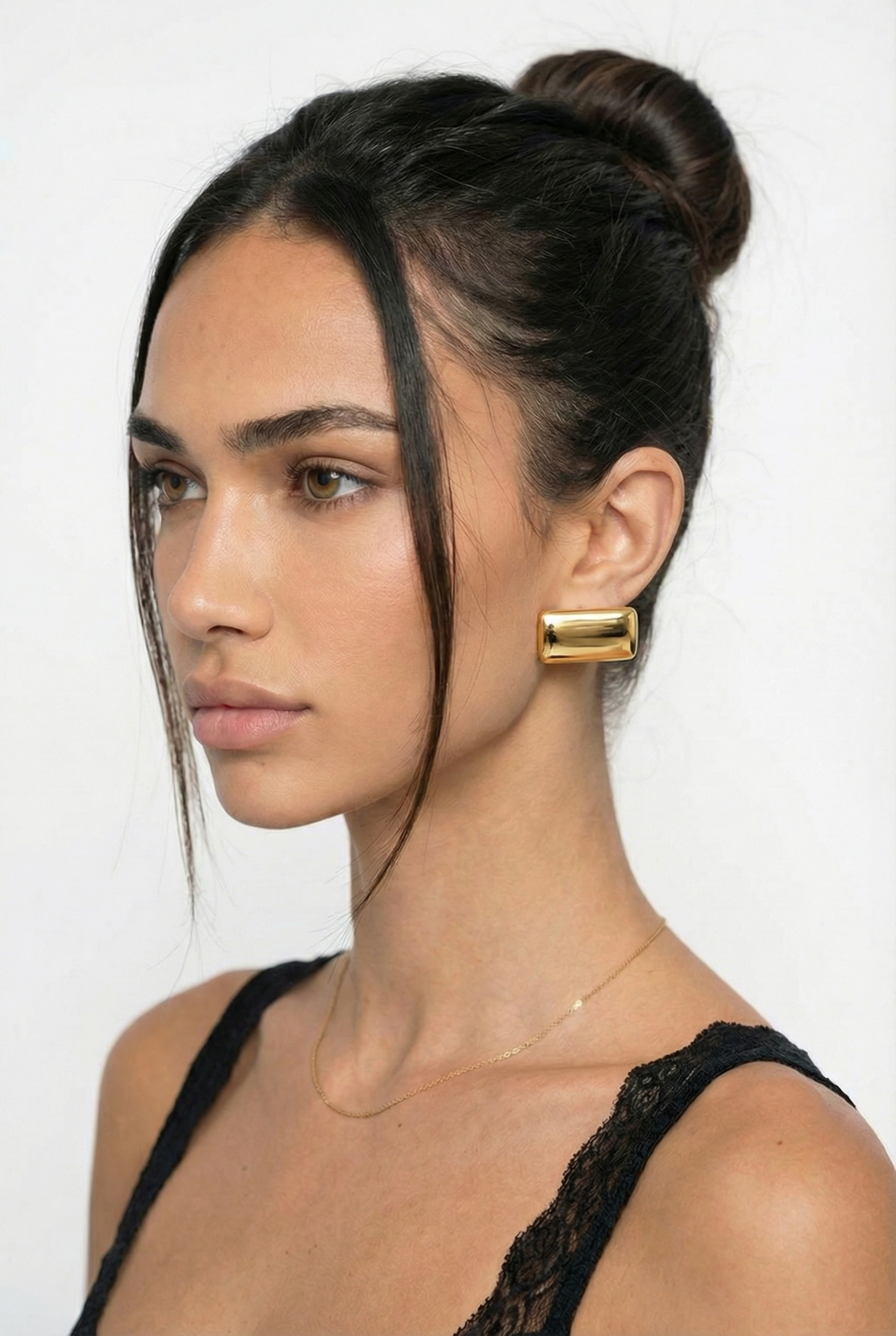 Woman with a stylish hair bun and gold earring on a white background