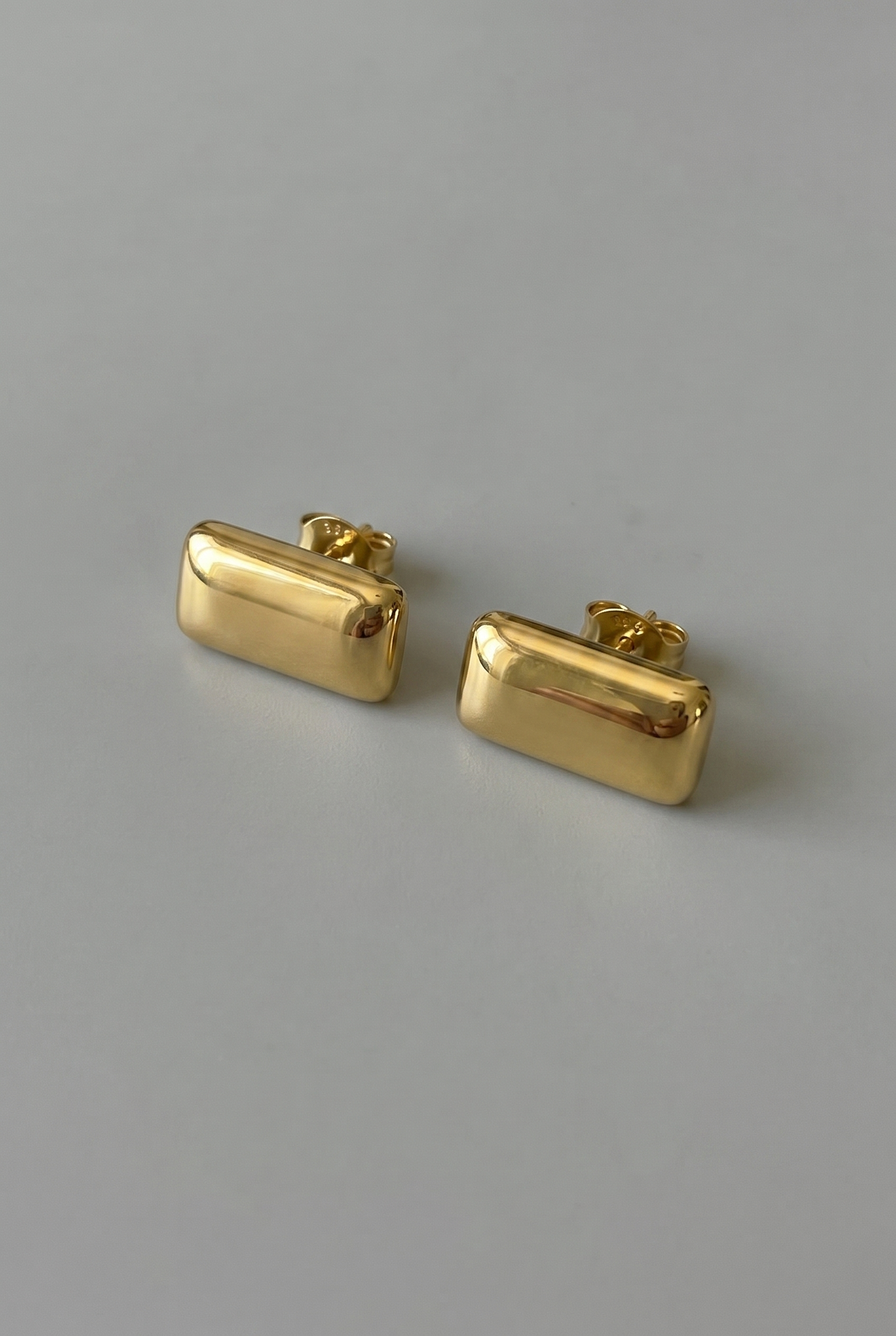 Pair of gold rectangular earrings on a gray background
