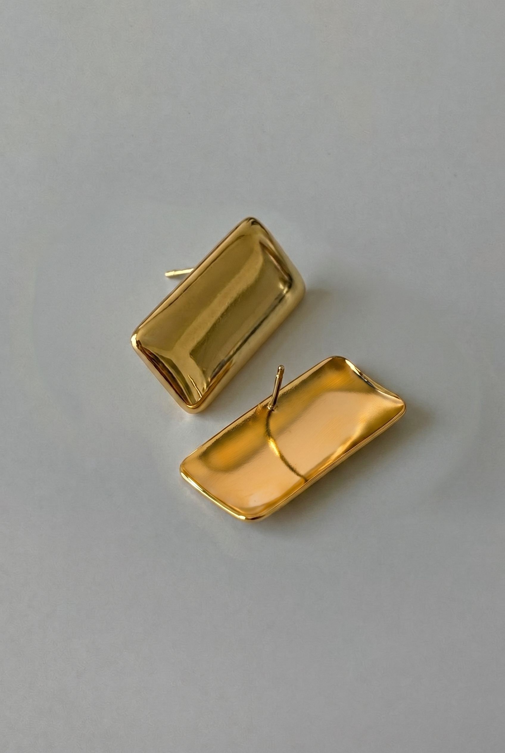 Gold rectangular earrings on a gray background