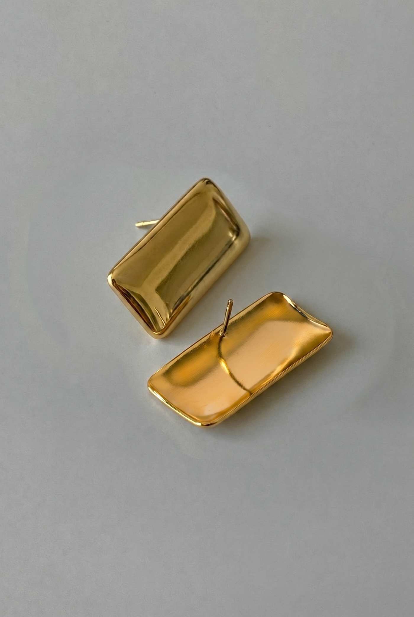 Gold rectangular earrings on a gray background