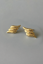 Gold wing-shaped earrings on a gray background